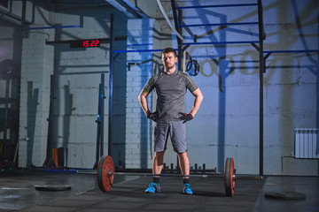 Strong man doing an exercise with a barbell in the gym on a background of a gray concrete wall