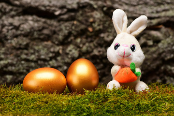 rabbit toy, golden easter eggs on green moss, tree bark