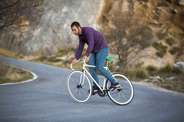 Cyclist man riding fixed gear sport bike in sunny day on a mountain road