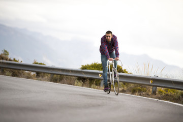 Cyclist man riding fixed gear sport bike in sunny day on a mountain road