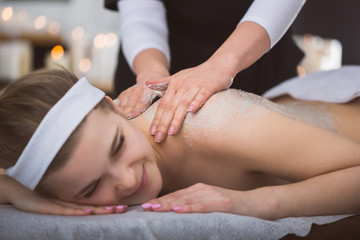Fototapeta na wymiar Young smiling woman getting firming sugar scrub therapy on her back