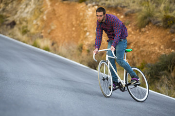 Cyclist man riding fixed gear sport bike in sunny day on a mountain road