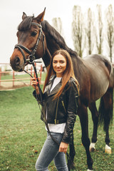 Beautiful girl communicates with the horse in the park. Preparing for the riding