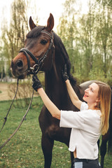 Beautiful girl communicates with the horse in the park. Preparing for the riding