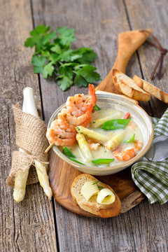 Spargelcremesuppe mit Garnelen und Zuckerschoten, mit getoastetem Butterbaguette rustikal serviert - Cream of asparagus soup with fried prawns and snow peas