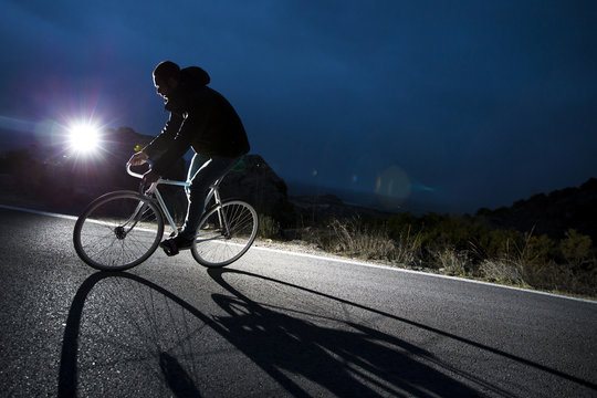 Cyclist man riding fixed gear sport bike in sunny day on a mountain road. Nocturne image.