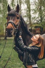 Obraz premium Beautiful girl communicates with the horse in the park. Preparing for the riding