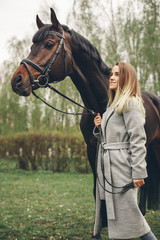 Obraz premium Beautiful girl communicates with the horse in the park. Preparing for the riding