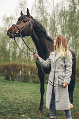 Obraz premium Beautiful girl communicates with the horse in the park. Preparing for the riding