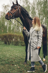 Obraz premium Beautiful girl communicates with the horse in the park. Preparing for the riding
