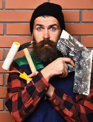 bearded foreman holding various building tools with surprised face