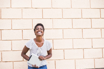 Smiling African American woman holding digital tablet near concrete wall