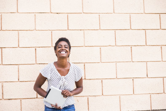 Smiling African American woman holding digital tablet near concrete wall