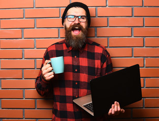 Bearded brutal caucasian hipster holding laptop with cup