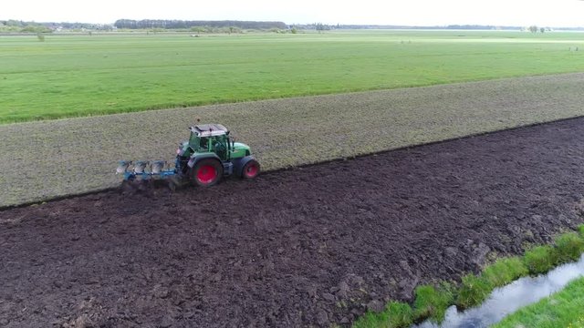 Aerial of modern tractor ploughing also known as plowing land a plough or plow is tool farm implement used in farming for cultivation of soil in preparation for sowing seed planting to loosen soil