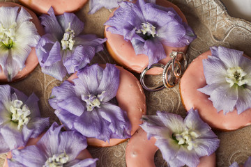 Wedding rings lie among pink cookies on the tray