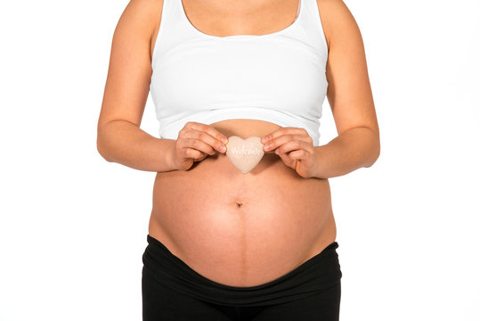Pregnant woman holding heart in front of her bare belly