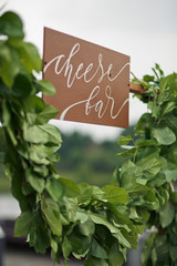 Wooden board with lettering 'Cheese bar' hangs over green garland