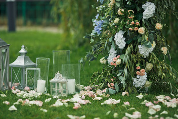 Glass vases and lanterns with candles stand on the lawn beneath wedding altar