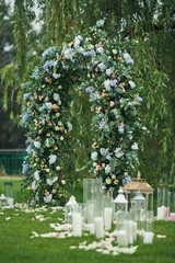 Decorative lanterns and vases with candles stand before green wedding altar