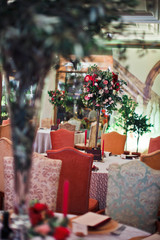 Cosy chairs stand at round tables decorated with red flowers