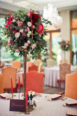 Cosy chairs stand at round tables decorated with red flowers