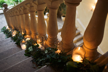Vases with shiny candles stand on the stairs with green garland