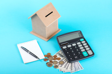 The concept of financial savings to buy a house. Money box, dollars, coins and calculator isolated on blue background.