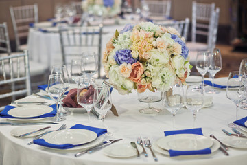 Glass vase with bouquet of white and blue flowers stands in the middle of dinner table