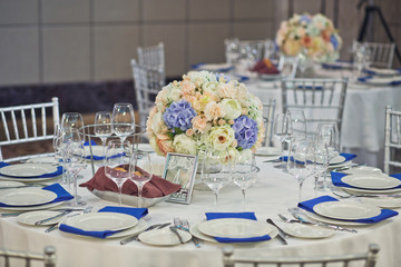 Glass vase with bouquet of white and blue flowers stands in the middle of dinner table