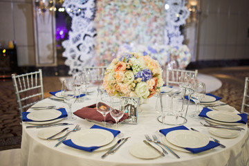 Bouquet of roses stands in the middle of dinner table with blue serviettes