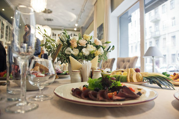 Plate with salad stands before vase with white roses on the table