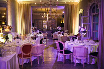 White chairs stand at round dinner tables in long restaurant hall