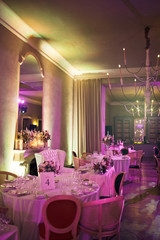 White chairs stand at round dinner tables in long restaurant hall