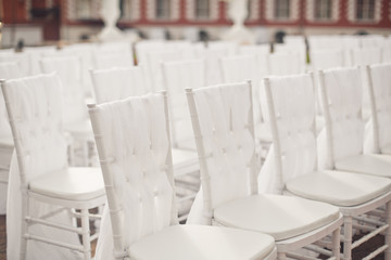 White chairs covered with white cloth stand in the rows outside