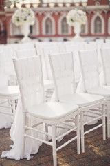 White chairs covered with white cloth stand in the rows outside