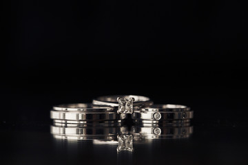 Engagement ring and wedding rings lie on each other on black background