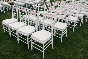 Fototapeta na wymiar White chairs stand in the row on green lawn