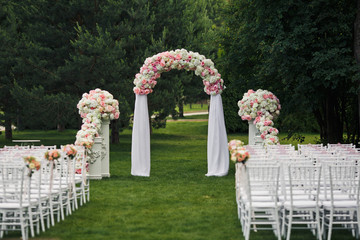 Wedding altar decorated with pink peonies stands on the lawn before the chair