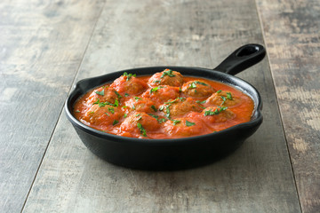 Meatballs with tomato sauce in iron frying pan on wooden table