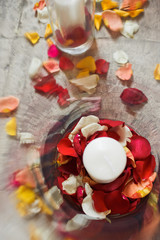 Look from above at white candle standing on red and yellow rose petals