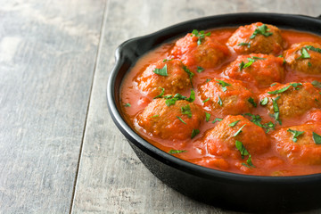 Meatballs with tomato sauce in iron frying pan on wooden table