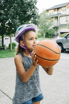 Girl With Helmet Playing Basketball On Driveway