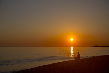 Beautiful scene with fisherman silhouette with rod sitting on sea beach