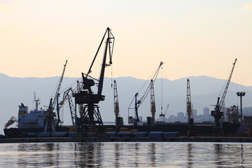 Silhouette of port cranes and a bulk carrier ship in the harbor with Ucka mountain, Istria, in the background at sunset, city of Rijeka, Croatia, Europe