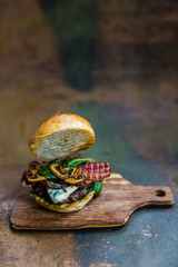 Tasty grilled beef burger with spinach lettuce and blue cheese served on wooden table with copyspace, blackboard in background.
