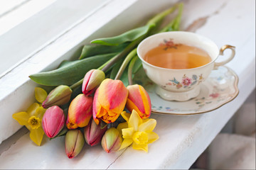 Tulips, daffodils and a cup of tea on the wooden windowsill. Selective focus.