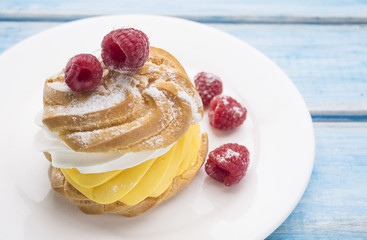 Biscuit cake with raspberry berries on a white plate. On blue wooden table.