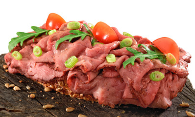 Thinly sliced rare roast beef open sandwich on wholegrain bread. Rocket, tomato and spring onion garnish.