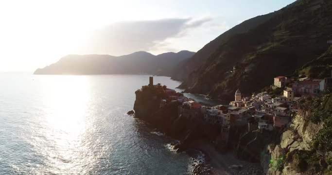 aerial view of travel landmark destination Vernazza, a small mediterranean sea town, Cinque terre National Park, Liguria, Italy. Sunset with cloud and flare. 4k aerial drone backward video shot
